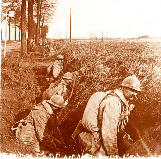 Soldiers setting up in a fox-holes along the roadside. They wear assault rolls tied around their chests.