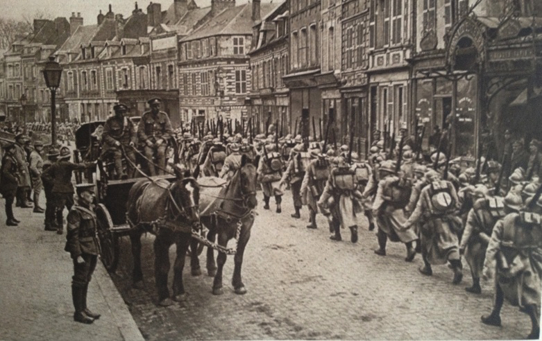 A column of French infantry marches past a group of British troops. 