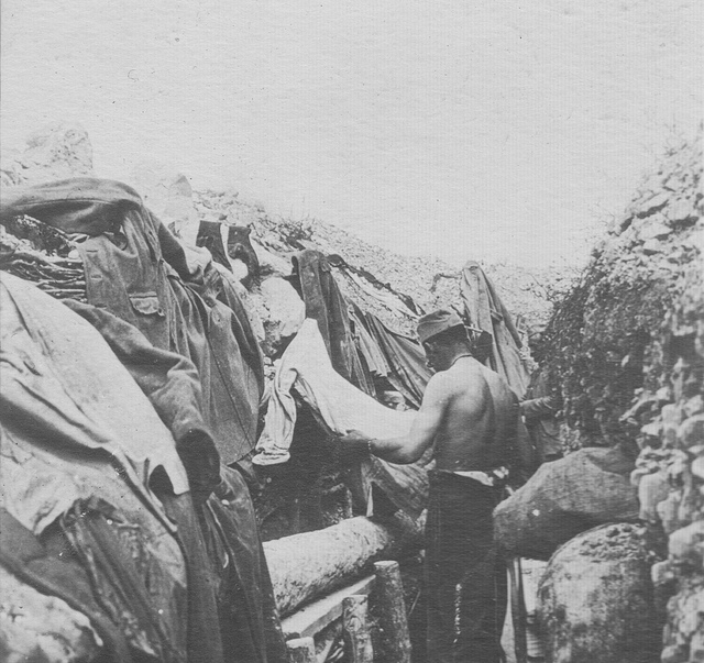 A soldier combs his clothes for lice beside his trench shelter.