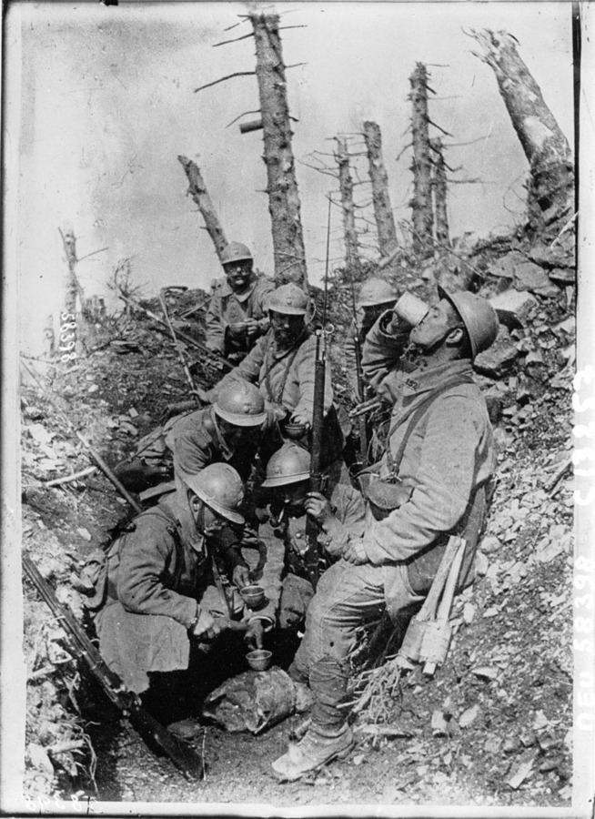 Men of the 152 RI rest after an attack in Argonne and share a cup of pinard. Note the early style raquette grenades suspended from the belt of the man on the right and the shell lodged in the tree.
