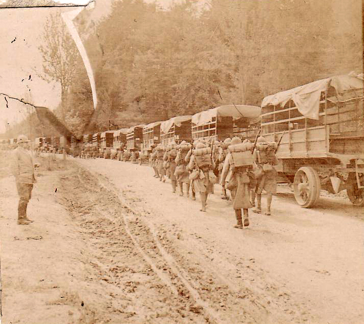 Troops march by a idle convoy of trucks.
