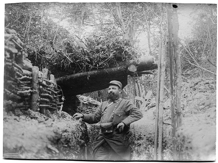 A man stands in front of a trench shelter, 1914.