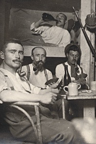 Soldiers playing cards and smoking pipes in a shelter.