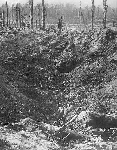 A soldiers stands in the bottom of a crater made by a large caliber shell.